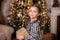 Close Up portrait Happy little girl with christmas present at home. Small Girl holds gift near Christmas tree on lights background