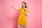 Close-up portrait of happy young woman in yellow dress and headphones pointing with finger, looking aside