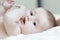 Close up portrait of infant sucking thumb and lying on white bed