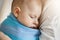 Close up portrait of innocent little child, sleeping on mother hands in blue baby sling. Quite and relaxing scene