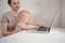 Close up portrait little baby boy funny facial expression sitting on mother`s lap studying laptop. Young mom work from home with