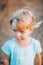 Close up portrait of little blonde girl with blue eyes outside with tousled hair and dirty face. Childhood in the country. Summer