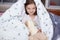 Close up portrait of little cheerful girl hides under blanket with fluffy dog toy, sweet, adorable child having fun on bed under