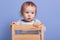 Close up portrait of little child looking aside, standing on chair isolated over blue background in studio, wearing striped