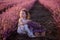 Close-up portrait of little girl sitting in field among rows, collecting bouquet of purple lavender