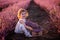 Close-up portrait of little girl sitting in field among rows, collecting bouquet of purple lavender