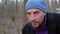 Close-up portrait of a man who smokes and drinks tea from a metal mug in the forest, looks into the camera.