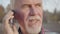 Close-up portrait of mature Caucasian man standing in the autumn park and talking by smart phone. Senior European guy