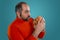 Close-up portrait of a middle-aged man with beard, dressed in a red turtleneck, posing with burgers against a blue