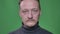 Close-up portrait of middle-aged man with beard watching into camera with no emotions on green background.