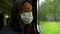 A close-up portrait of a middle-aged woman riding a train and looking out the window, wearing a gray hood and a