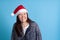 close up portrait of mischievous Asian young woman in Santa hat smiling and biting lip with her teeth on blue background