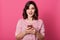 Close up portrait of modern women holding cellphone isolated over pink background, slim female dresses casual outfit, keeps mouth