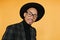 Close-up portrait of mulatto male model in black hat. Indoor photo of cheerful young man with brown skin..