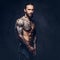 Close-up portrait of a muscular naked bearded tattoed male with a stylish haircut, isolated on a dark background.