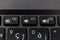 A close up portrait of the mute, volume up and volume down buttons on a laptop keyboard. The physical keys are black with a white