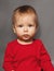 Close-up portrait of a nine-month-old baby girl with blond hair and blue eyes, dressed in a red bodysuit on a gray background