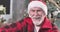 Close-up portrait of old Caucasian man in red Christmas hat looking at camera and winking. Positive Santa Claus posing