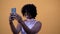Close up and portrait of one young and beautiful afro American woman using her phone smiling and having fun with yellow wall at th