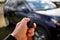A close up portrait of a person standing next to a car holding a car key in his hand pressing the unlock button. the remote