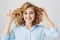 Close-up portrait of playful attractive woman with frizzle hairstyle holding her curly hair and smiling joyfully at