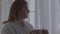 Close up portrait of plump girl in white bathrobe standing near large floor-to-ceiling window with cup of coffee or tea