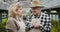 Close-up portrait of positive mature caucasian man in straw hat and blond woman talking and smiling in greenhouse