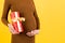 Close up portrait of pregnant woman in brown dress holding a gift box at yellow background. Pregnancy celebration. Copy space