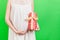 Close up portrait of pregnant woman in white dress holding a gift box at green background. Pregnancy celebration. Copy space
