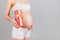 Close up portrait of pregnant woman in white underwear holding a gift box at gray background. Pregnancy celebration. Copy space