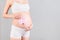 Close up portrait of pregnant woman in white underwear holding pink socks for a baby girl at gray background. Waiting for a child