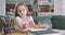 Close-up portrait of pretty Caucasian girl counting on fingers and writing result into exercise book. Smart schoolgirl