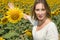Close up portrait of a pretty woman looks at the camera as she shows a field of sunflowers behind her. She has a large sunflower