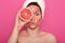 Close up portrait of pretty woman with perfect skin,posing with facial mask, holding half of grapefruit in front of her eye, lady