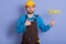 Close up portrait of repairman wearing yellow protective hat, apron and uniform, holding paint roller for painting wall and