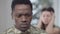 Close-up portrait of sad African American man looking at camera as blurred furious Caucasian wife yelling gesturing at