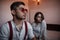 Close-up portrait of a sad brooding brunette guy in sunglasses. in the background on the bed a young brunette girl. selective