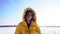 Close-up portrait of a sad curly-haired schoolgirl walking in a snowy field in a yellow hooded coat. Loneliness and