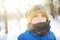 Close-up portrait of sad little boy in blue winter clothes walks during a snowfall on cold day. Outdoors winter activities for