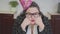 Close up portrait sad plump woman in a birthday cap and stylish glasses sitting at the table in the kitchen. The fat