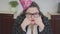 Close up portrait sad plump woman in a festive cap and stylish glasses sitting at the table in the kitchen. The fat lady