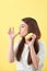 Close up portrait of a satisfied pretty girl eating donuts isolated over yellow background