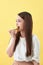 Close up portrait of a satisfied pretty girl eating donuts  over yellow background