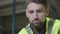 Close-up portrait of serious Caucasian man in green vest looking down. Professional worker working at manufacture plant