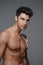 Close-up portrait of a sexy brunette male model with a bare torso against a gray background