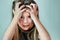 Close-up portrait of shocked unhappy little girl with long hair holding her head in hands