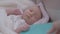 Close-up portrait sleeping little baby girl lying in bed with female hand trying take tablet. Relaxed carefree adorable