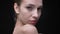 Close-up portrait of slim caucasian girl touching gently her neck and turns to camera on black background.