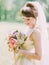 Close-up portrait of the smiling bride looking down and holding the wedding bouquet of colourful peonies. Park location.