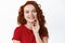 Close up portrait of smiling happy woman with ginger curly hair, touching pale smooth and healthy skin with fingertips